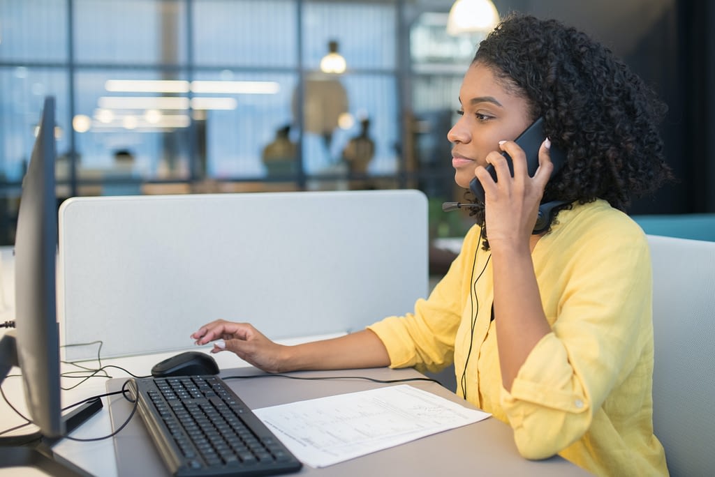 black woman at desk in yellow shirt talking on phone